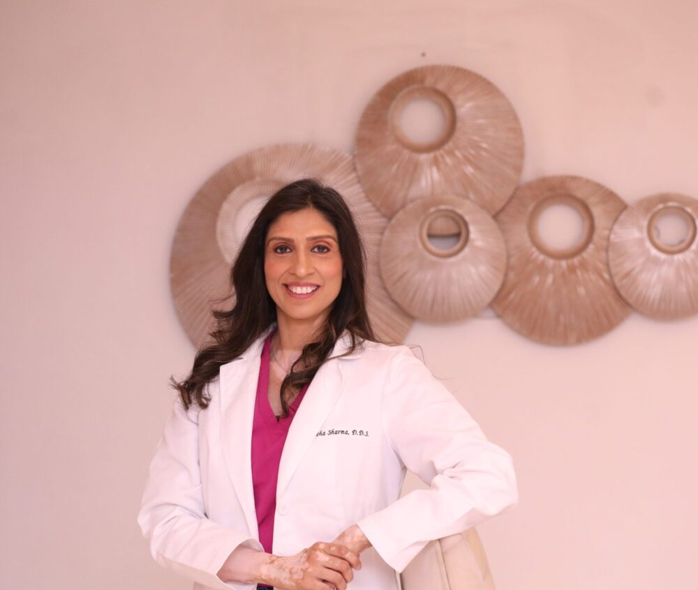 Dr. Neha Sharma in a dental clinic setting, smiling and wearing a white coat, with dental-themed decor in the background, representing personalized dental care at Dental Krafts in Sacramento.