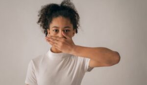 Person smiling with hand covering mouth, suggesting concerns about bad breath and oral hygiene.