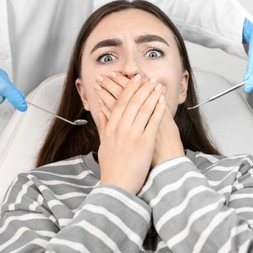 Woman with long hair covering her mouth, expressing anxiety or discomfort, representing the importance of sedation dentistry for stress-free dental visits.